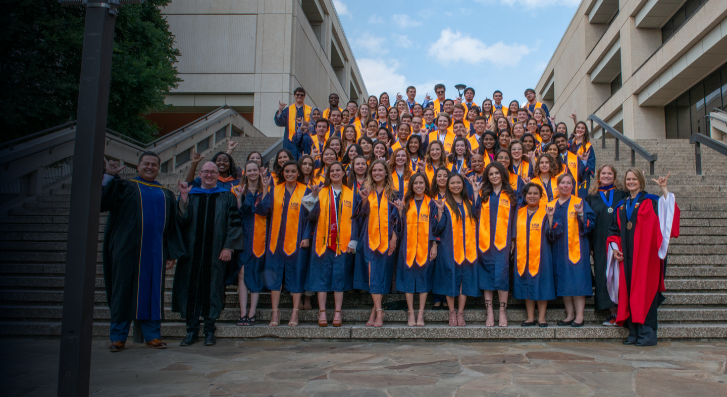 Group of students in caps and gowns posing on stairs