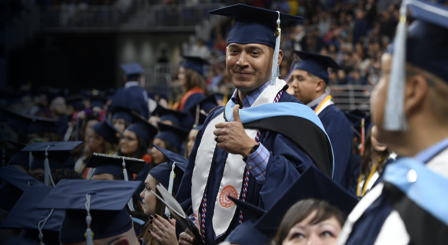 Graduating student giving a thumbs up at ceremony